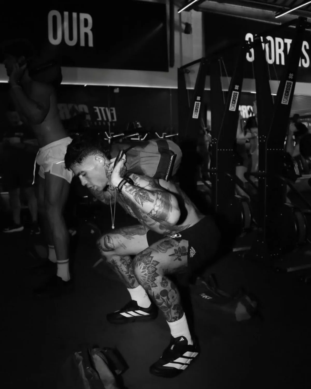 Caio Cabral setting up under a barbell in a dark gym, wearing the Adizero Dropset